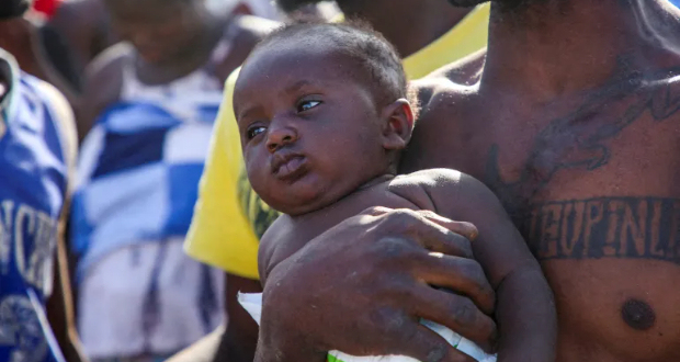 A refugee from Africa carries a child near the Libyan-Tunisian border in Ras Ajdir, Libya, on July 23, 2023 [Hazem Ahmed/Reuters]